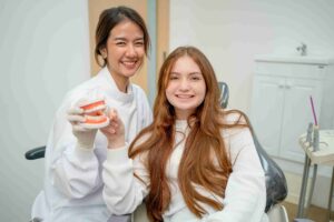 Teen patient and dental professional smiling during a dental consultation with a tooth model.